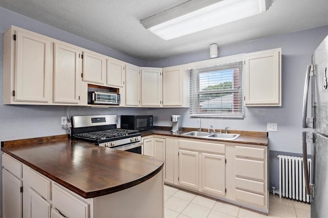 kitchen with radiator, sink, stainless steel gas range, light tile patterned flooring, and white cabinetry