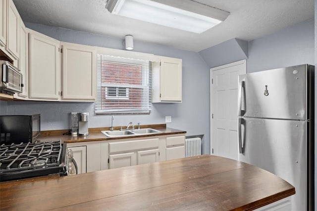 kitchen featuring wooden counters, radiator heating unit, sink, appliances with stainless steel finishes, and white cabinetry