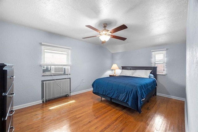 bedroom featuring ceiling fan, radiator heating unit, hardwood / wood-style floors, vaulted ceiling, and multiple windows