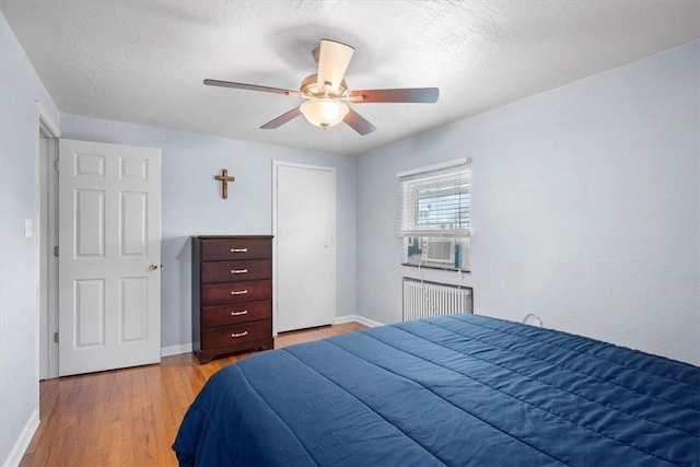 bedroom with light wood-type flooring, radiator, a textured ceiling, cooling unit, and ceiling fan