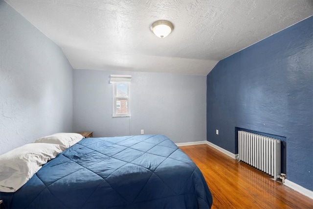 bedroom with a textured ceiling, radiator, vaulted ceiling, and hardwood / wood-style flooring