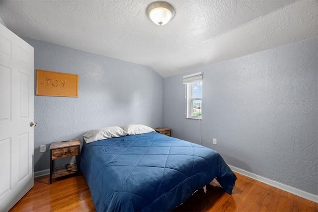 bedroom featuring hardwood / wood-style floors, a textured ceiling, and vaulted ceiling