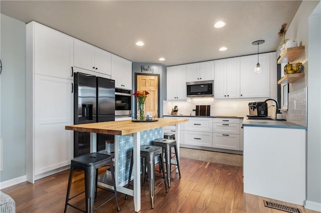 kitchen with pendant lighting, sink, appliances with stainless steel finishes, dark hardwood / wood-style flooring, and white cabinetry