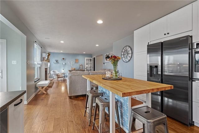 kitchen with butcher block countertops, a kitchen breakfast bar, stainless steel fridge, and white cabinetry