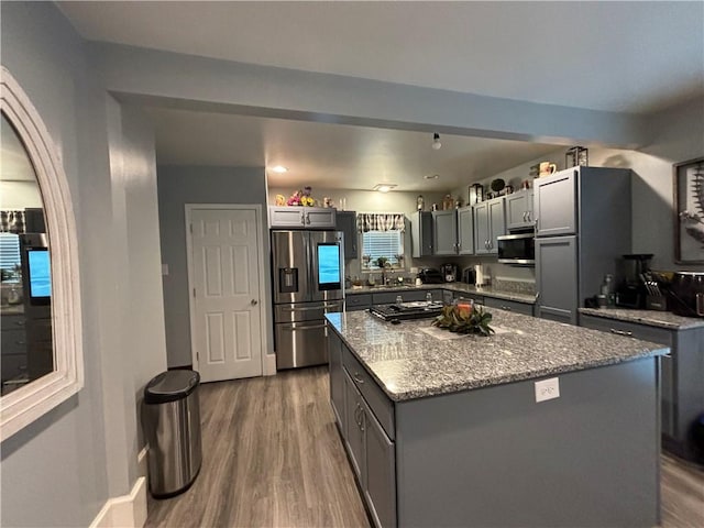 kitchen featuring light stone countertops, appliances with stainless steel finishes, a center island, and gray cabinets