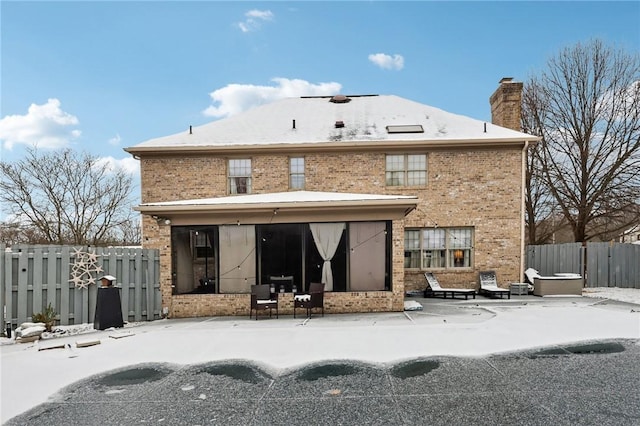 snow covered rear of property featuring a hot tub