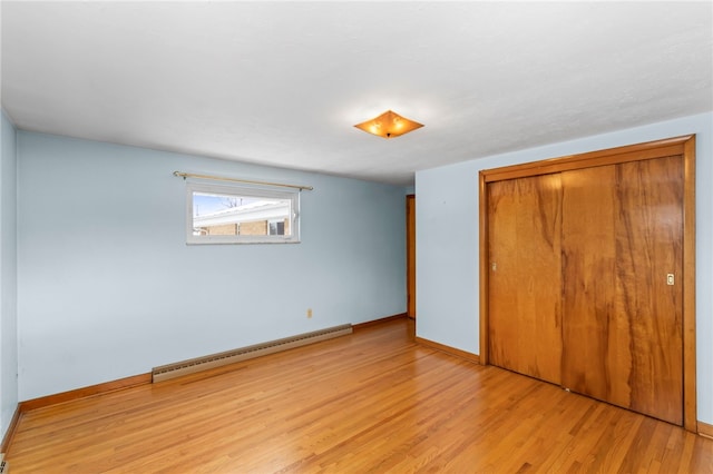 unfurnished bedroom featuring light hardwood / wood-style flooring, baseboard heating, and a closet