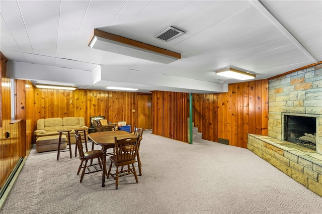 dining space featuring wood walls, a stone fireplace, light colored carpet, and baseboard heating