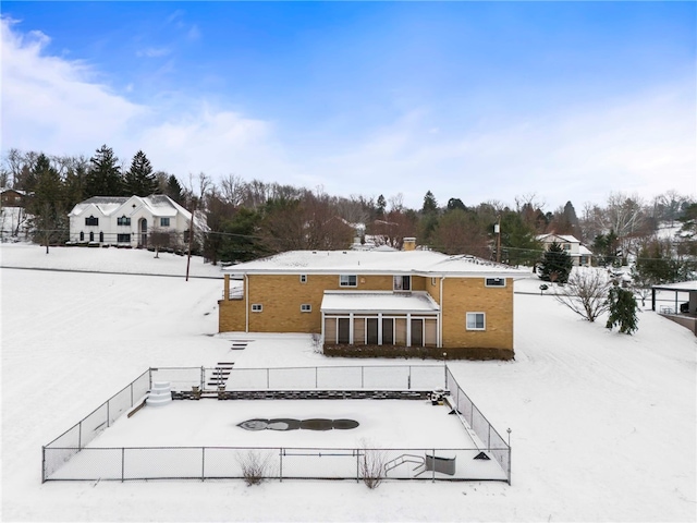 snow covered back of property featuring a sunroom