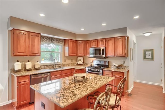 kitchen featuring light stone countertops, sink, light hardwood / wood-style flooring, a kitchen island, and appliances with stainless steel finishes