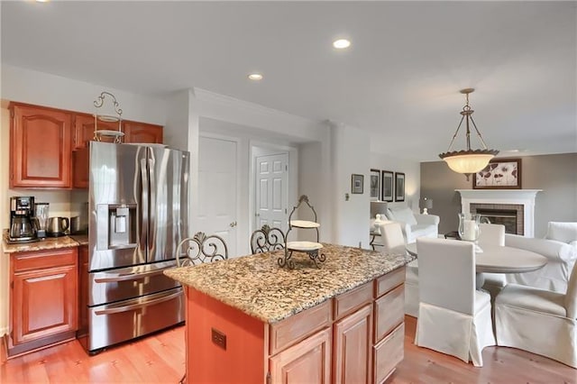 kitchen featuring stainless steel fridge, decorative light fixtures, a kitchen island, and light hardwood / wood-style floors