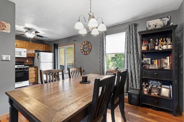 dining area with a textured ceiling, wood-type flooring, and ceiling fan with notable chandelier