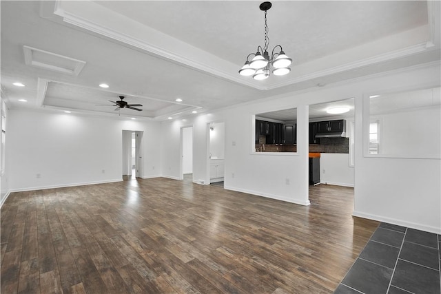 unfurnished living room featuring ceiling fan with notable chandelier, dark hardwood / wood-style flooring, and a tray ceiling