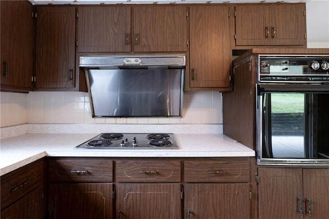 kitchen featuring tasteful backsplash, black oven, stainless steel gas cooktop, and range hood