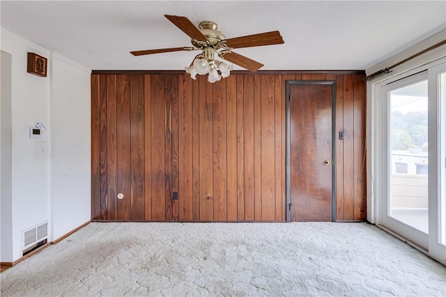 carpeted empty room with ceiling fan, wood walls, and crown molding