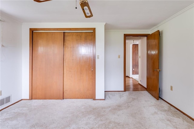 unfurnished bedroom with ceiling fan, a closet, light colored carpet, and crown molding