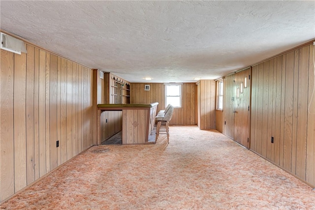 bar featuring wood walls, light colored carpet, and a textured ceiling