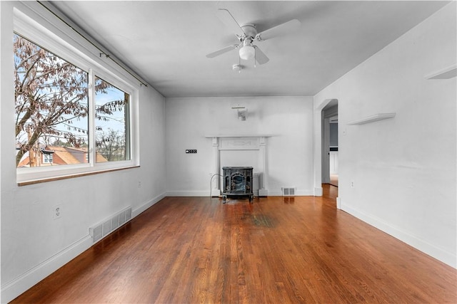 unfurnished living room with wood-type flooring, a wood stove, a wealth of natural light, and ceiling fan