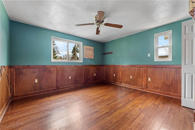 empty room featuring hardwood / wood-style floors, a wealth of natural light, ceiling fan, and wood walls