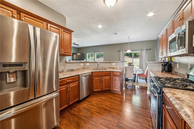 kitchen with light stone countertops, stainless steel appliances, hanging light fixtures, and sink