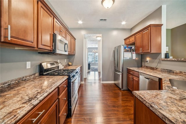 kitchen with light stone countertops, stainless steel appliances, and dark wood-type flooring