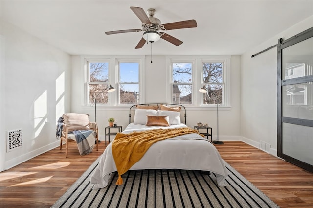 bedroom featuring wood-type flooring, a barn door, and ceiling fan