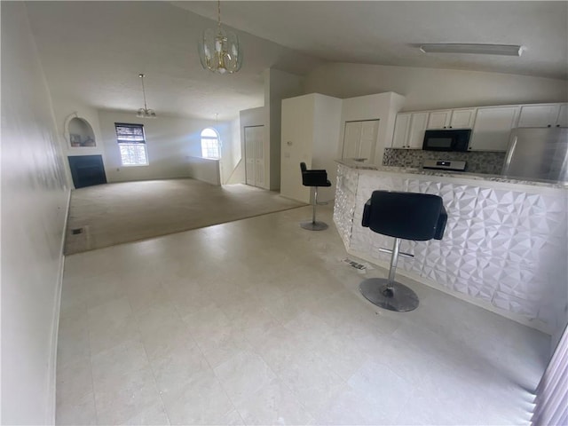 kitchen with refrigerator, hanging light fixtures, light stone countertops, tasteful backsplash, and white cabinetry