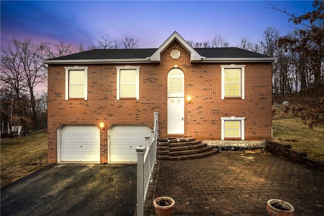 bi-level home featuring a garage, brick siding, roof with shingles, and aphalt driveway