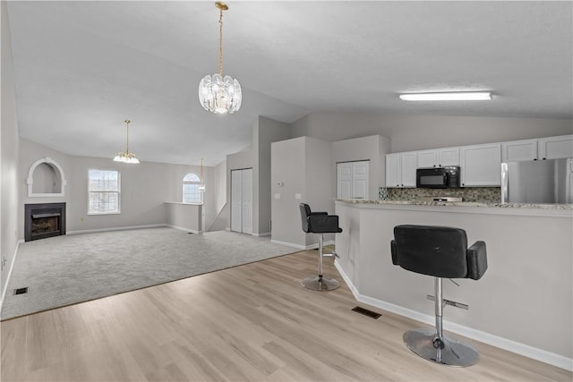 kitchen with open floor plan, freestanding refrigerator, white cabinetry, a kitchen bar, and black microwave