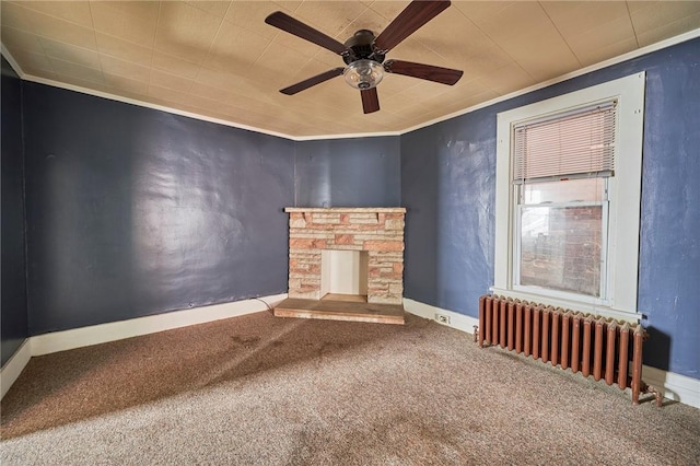 unfurnished living room featuring radiator, a stone fireplace, crown molding, carpet flooring, and ceiling fan