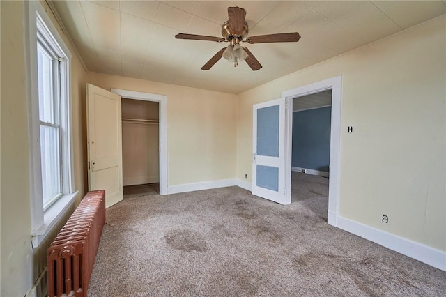 unfurnished bedroom featuring carpet flooring, ceiling fan, radiator, and a closet