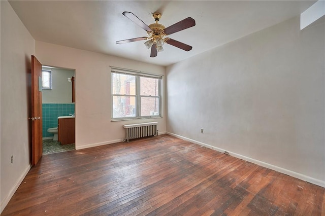 unfurnished room with ceiling fan, radiator heating unit, dark wood-type flooring, and tile walls