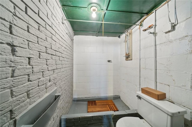 bathroom with toilet, walk in shower, and brick wall