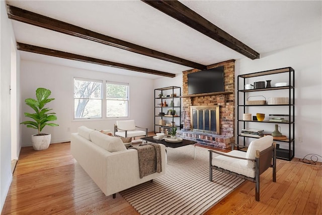 living room featuring beam ceiling, light wood-type flooring, and a brick fireplace