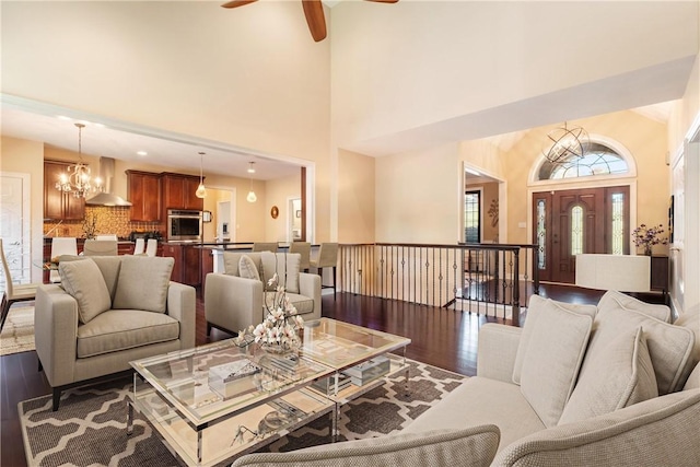 living room with ceiling fan with notable chandelier, beam ceiling, a towering ceiling, and dark wood-type flooring