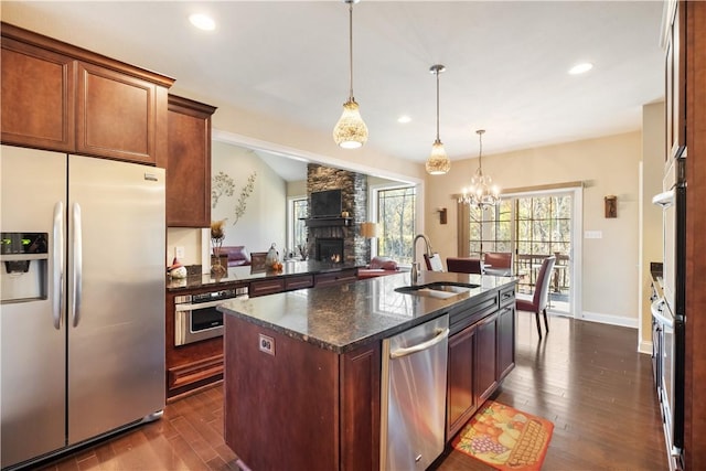 kitchen with sink, dark stone countertops, a fireplace, an island with sink, and stainless steel appliances