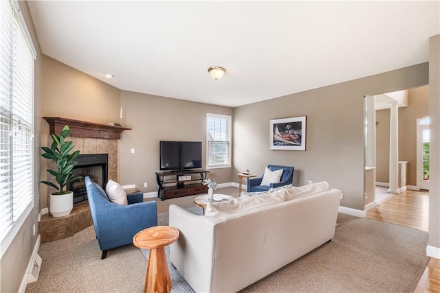 living room with decorative columns, a tiled fireplace, and light carpet