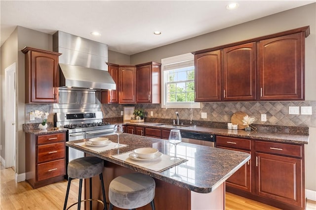 kitchen featuring appliances with stainless steel finishes, light wood-type flooring, sink, wall chimney range hood, and a kitchen island