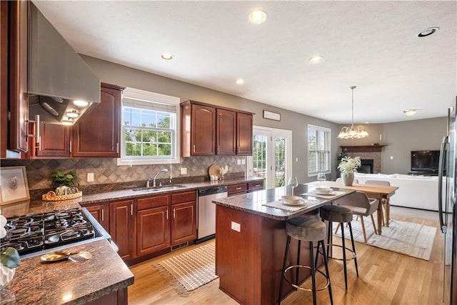 kitchen with appliances with stainless steel finishes, wall chimney exhaust hood, sink, a notable chandelier, and a center island