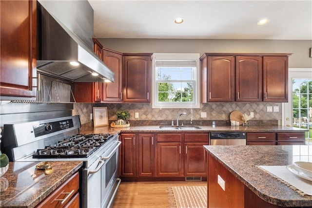 kitchen featuring dark stone countertops, sink, stainless steel appliances, and wall chimney range hood