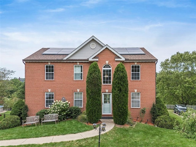 colonial inspired home featuring solar panels and a front lawn