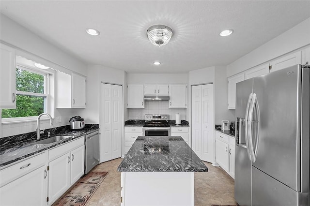 kitchen with appliances with stainless steel finishes, white cabinetry, a kitchen island, and dark stone countertops