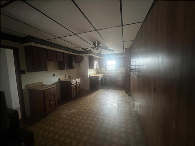 basement featuring a drop ceiling, ceiling fan, and wooden walls