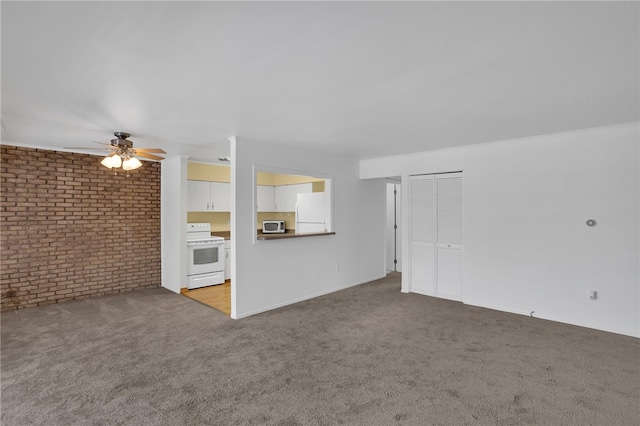 unfurnished living room featuring ceiling fan, carpet, and brick wall