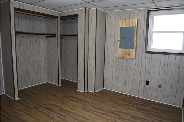 unfurnished bedroom featuring electric panel, a closet, dark wood-type flooring, and wood walls