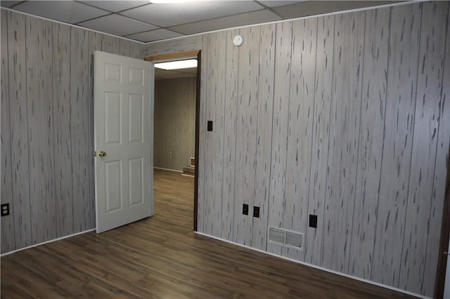 unfurnished room with a drop ceiling, wood-type flooring, and wooden walls