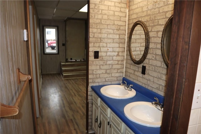 bathroom with vanity, hardwood / wood-style floors, a paneled ceiling, and brick wall