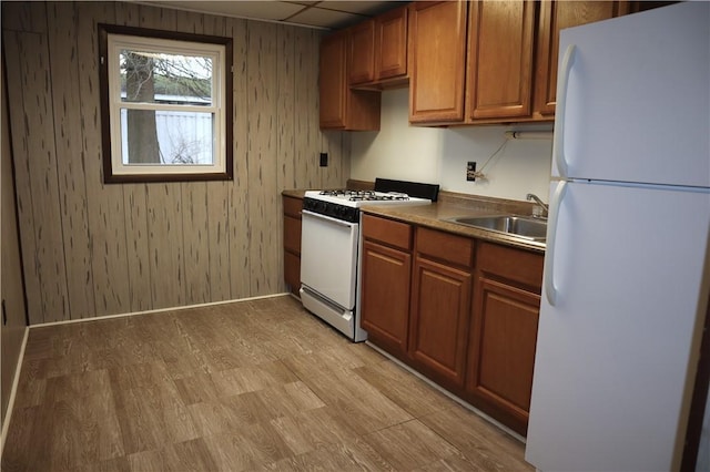 kitchen with light wood-type flooring, white appliances, sink, and wooden walls