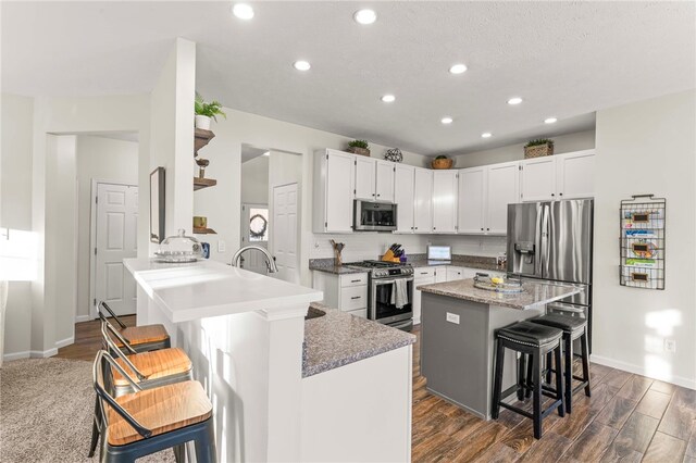 kitchen with light stone countertops, a center island, a breakfast bar area, white cabinets, and appliances with stainless steel finishes