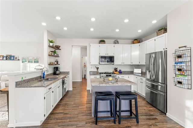 kitchen featuring appliances with stainless steel finishes, dark stone counters, a breakfast bar, sink, and white cabinets